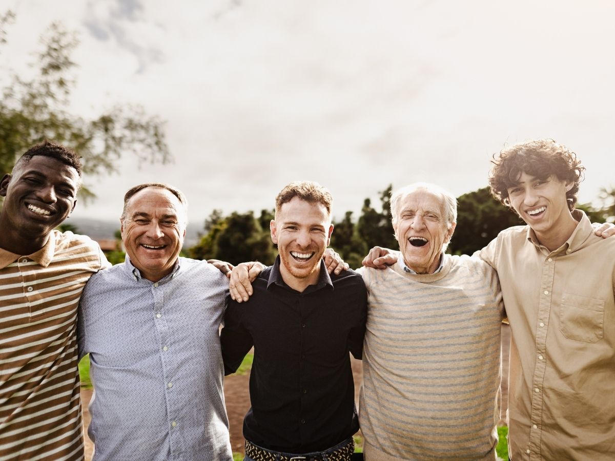 A diverse group of men smiling outdoors, representing community support and emotional wellness—an important part of managing stress alongside acupuncture treatments.