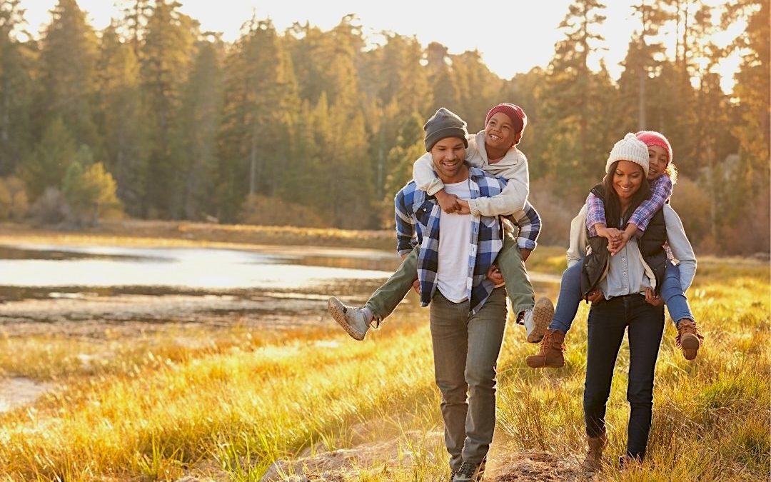 Happy family walking near a scenic lake and forest enjoying wellness and balance from acupuncture treatments.