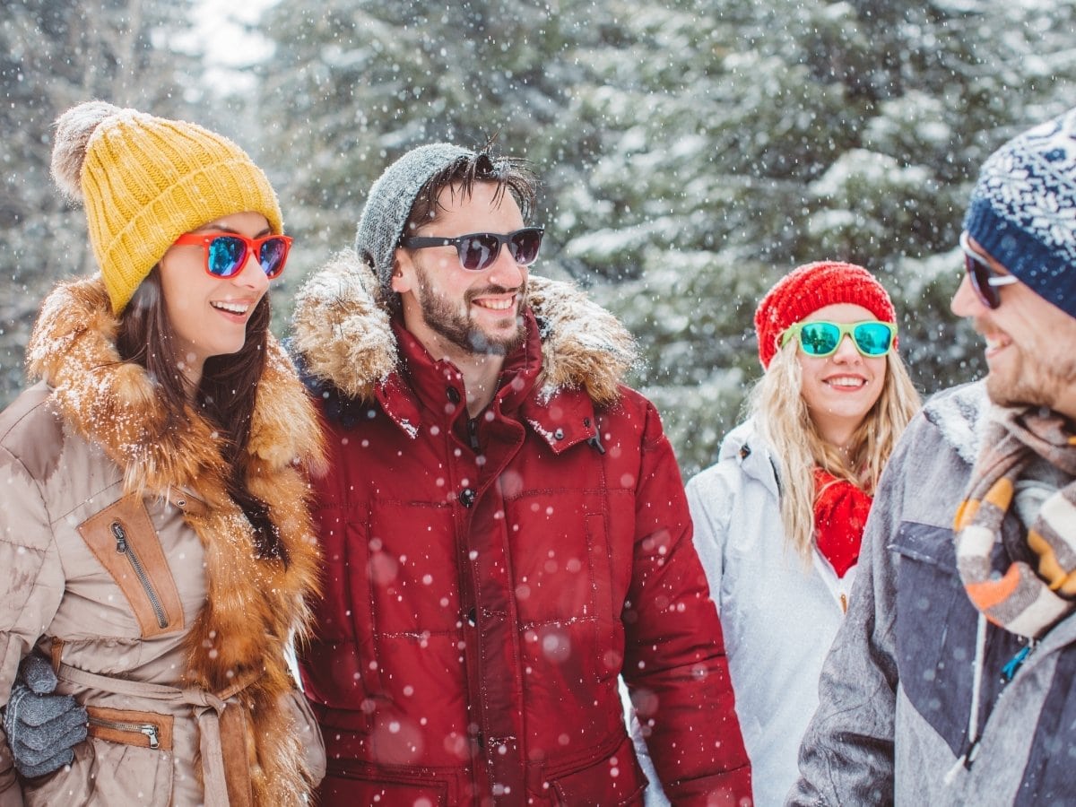 Group of friends dressed in light winter gear, laughing together outdoors on a snowy winter day.