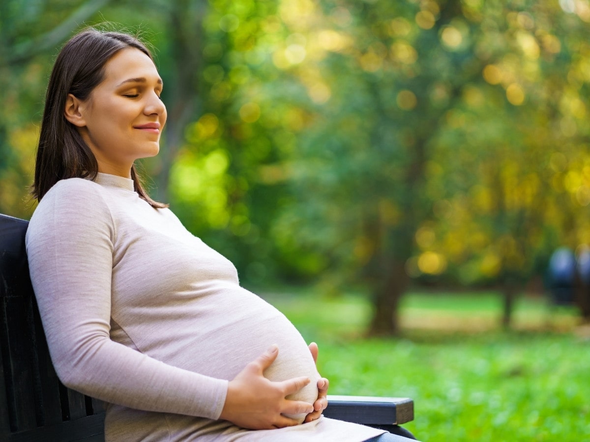 Peaceful woman sitting on a park bench with hands on her belly, reflecting calmness, balance, and the nurturing power of fertility.