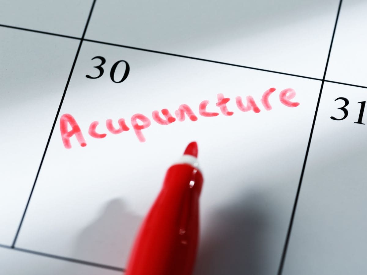 Zoomed-in calendar with acupuncture written in red and a pen pointing to it, representing planning for acupuncture therapy at Lim Acupuncture Clinic.