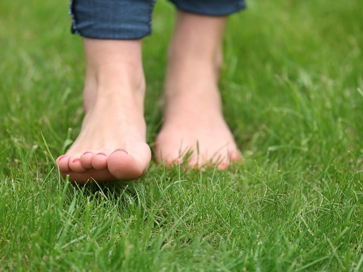 Person walking barefoot on grass, demonstrating foot sensation and common peripheral neuropathy symptoms.