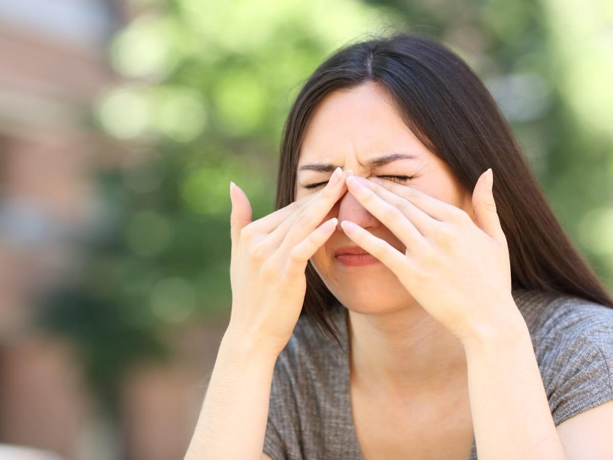 A women itching her eyes outside because of her Seasonal Allergies.